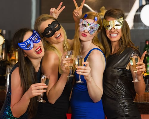 Attractive women wearing masks holding champagne looking at camera