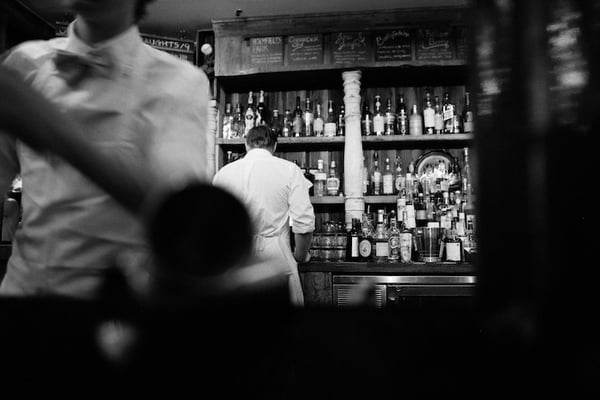 Black and white image of bar and with bar manager in background and bartender in foreground