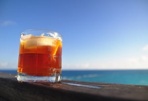 dark and stormy rum cocktail sitting on a railing on a sunny day by the ocean