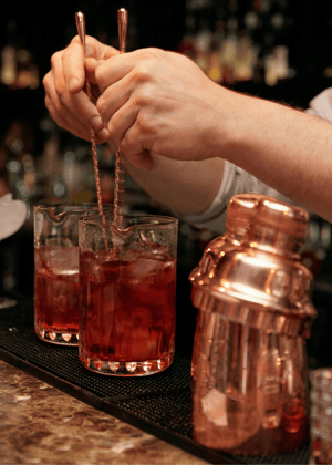 Bartender's hands mixing cocktail with two stirrers