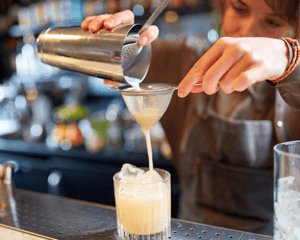 Bartender pouring cocktail through strainer into a rocks glass