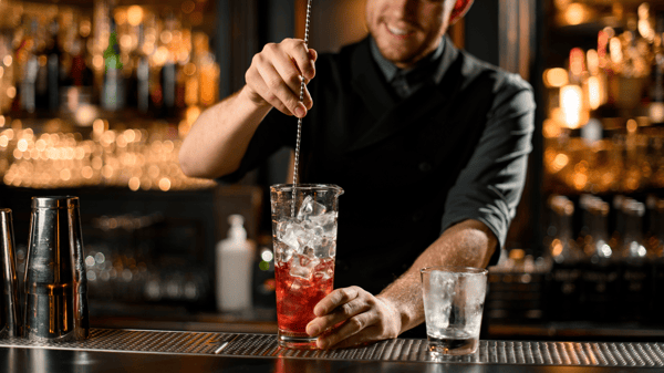 Bartender mixing red cocktail in tall glass with ice and a bar spoon