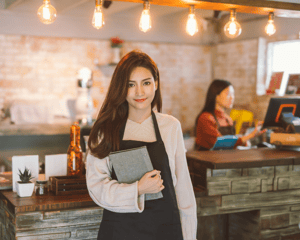 Woman wearing apron and holding book standing behind a bar and smiling