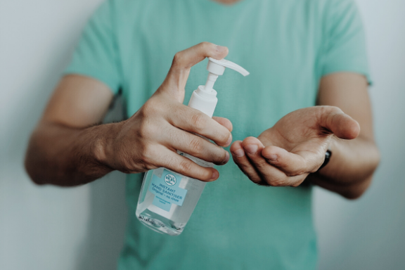 Man in green shirt on white background putting hand sanitizer on his hands