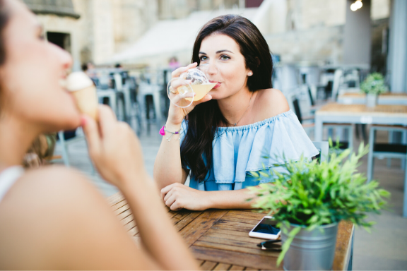 Woman drinking a cocktail with her friend at an outdoor patio