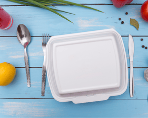 Photo of styrofoam take out container on a blue table with cutlery and fruit 