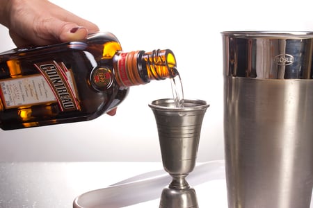 Bottle of Cointreau being poured into cocktail shaker next to cocktail shaker