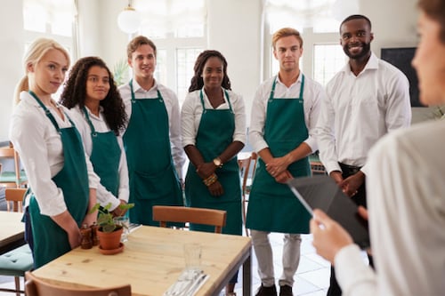 Group of employees standing in line wearing green aprons as manager talks to them