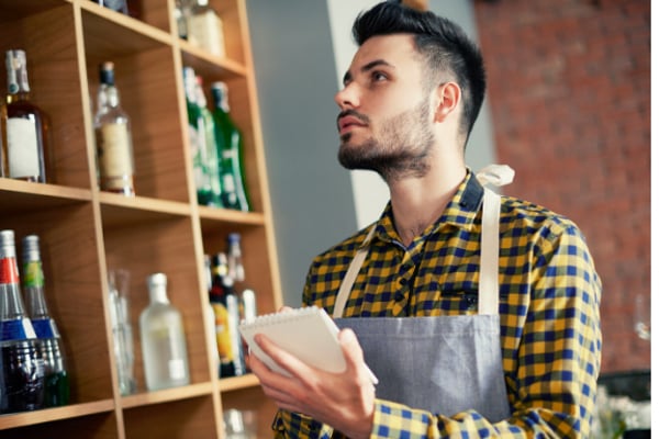 Man in checkered shirt holding a pen and pad taking bar inventory