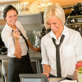 Two women behind the bar wearing work uniforms and laughing