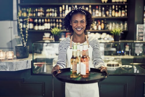 Woman holding tray of beers out and smiling in front of a bar