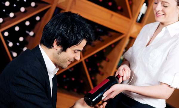 Restaurant waitstaff server showing bottle of red wine to male customer in a suit