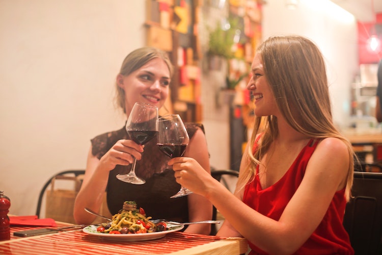 Two Smiling Women Clinking Red Wine in Wine Glasses Whule Sharing Dinner at a Restaurant